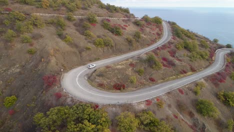 white crossover car goes on serpentine mountain road. aerial view. drone is following vehicle.