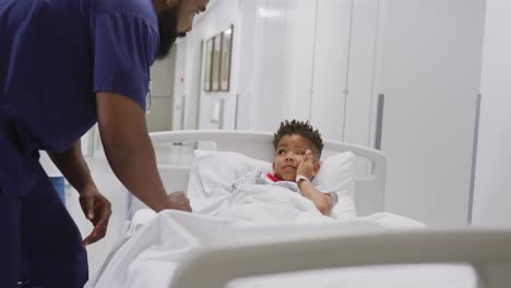 african american male doctor talking to child patient laying in bed at hospital