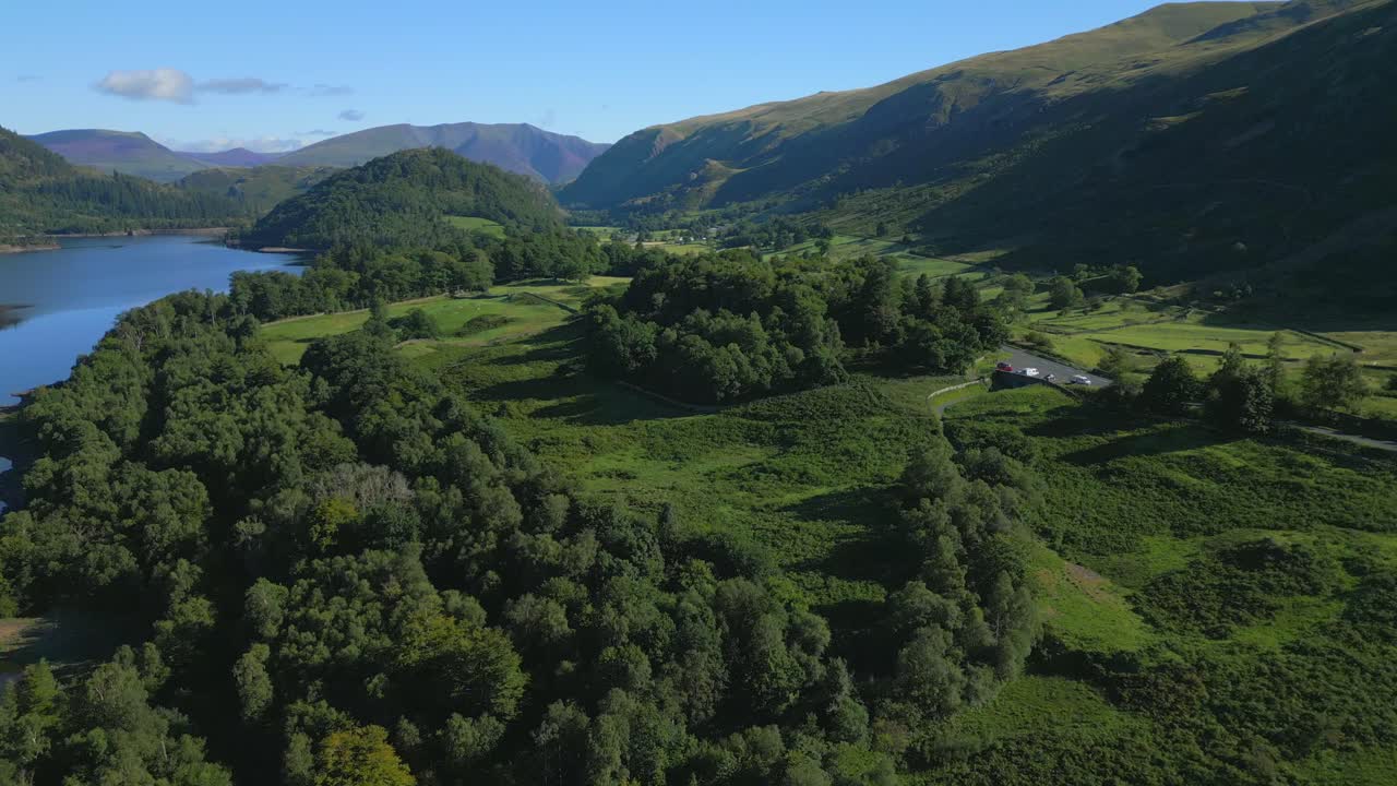 Flying over lakeside woodland towards mountains on sunny summer morning at Thirlmere, English Lake District, Cumbria, UK