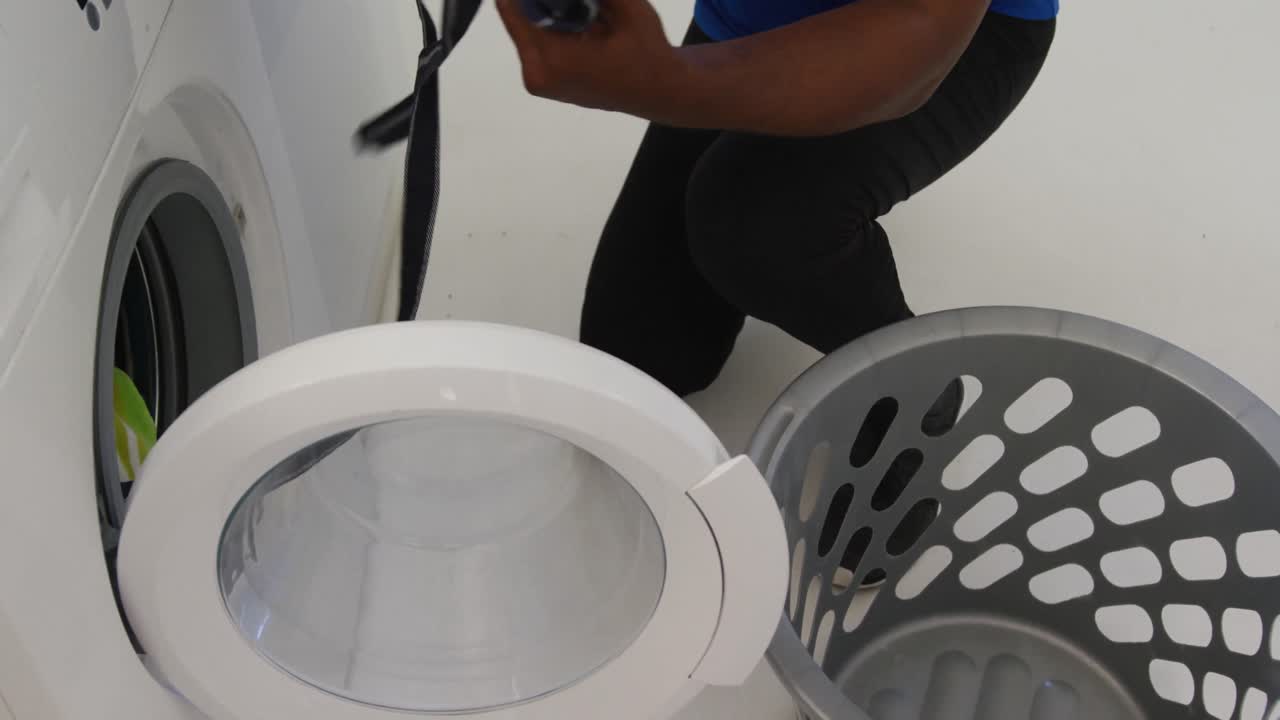 아프리카계 미국인 노인 이 집 에서 세탁기 에서 깨 ⁇  한 세탁물을 꺼내고 있다