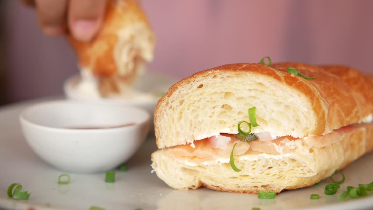 persona comiendo un sándwich de croissant con salmón y queso crema
