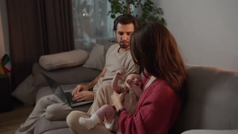 A-little-baby-girl-in-a-brown-and-white-T-shirt-is-crying-and-her-young-mother-is-calming-the-little-girl-while-sitting-on-the-sofa-with-her-husband-in-a-modern-apartment