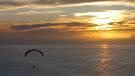 silhouette of paraglider over ocean with beautiful golden sunset reflecting on the water