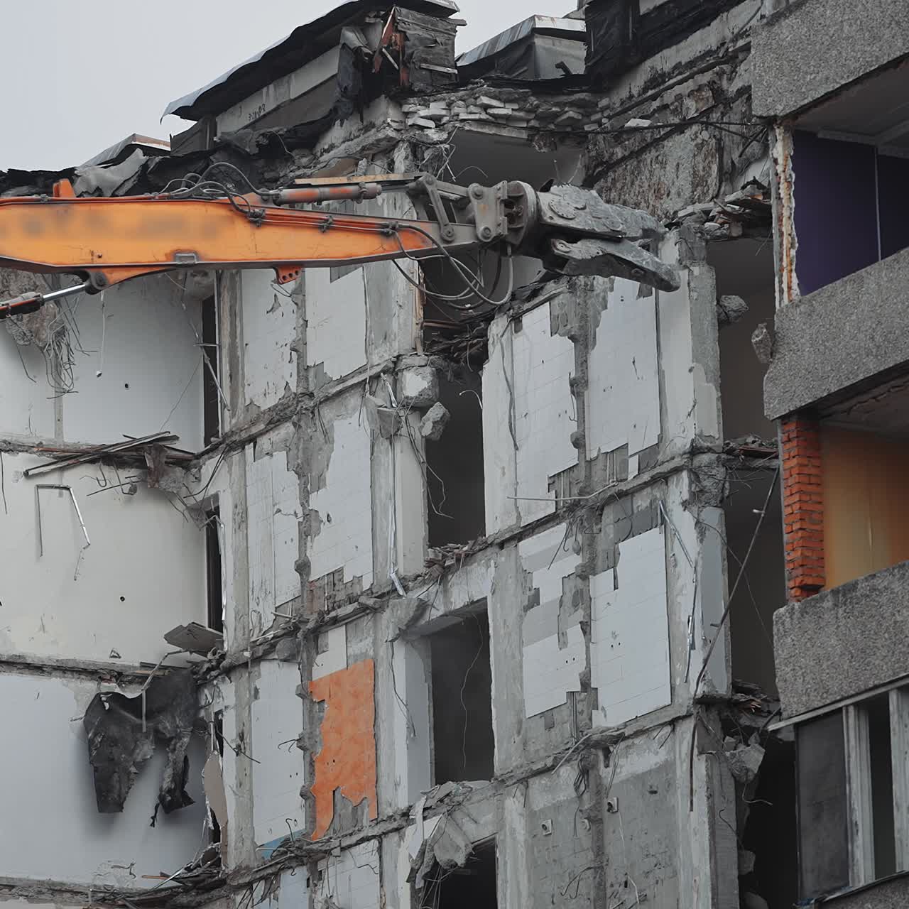 Big hydraulic claw grasps the concrete floor of the destroyed house. Excavator crasher reaches high to break the walls and floors of the ruined building
