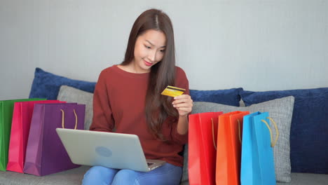 smiling asian woman shopping online with credit card and laptop