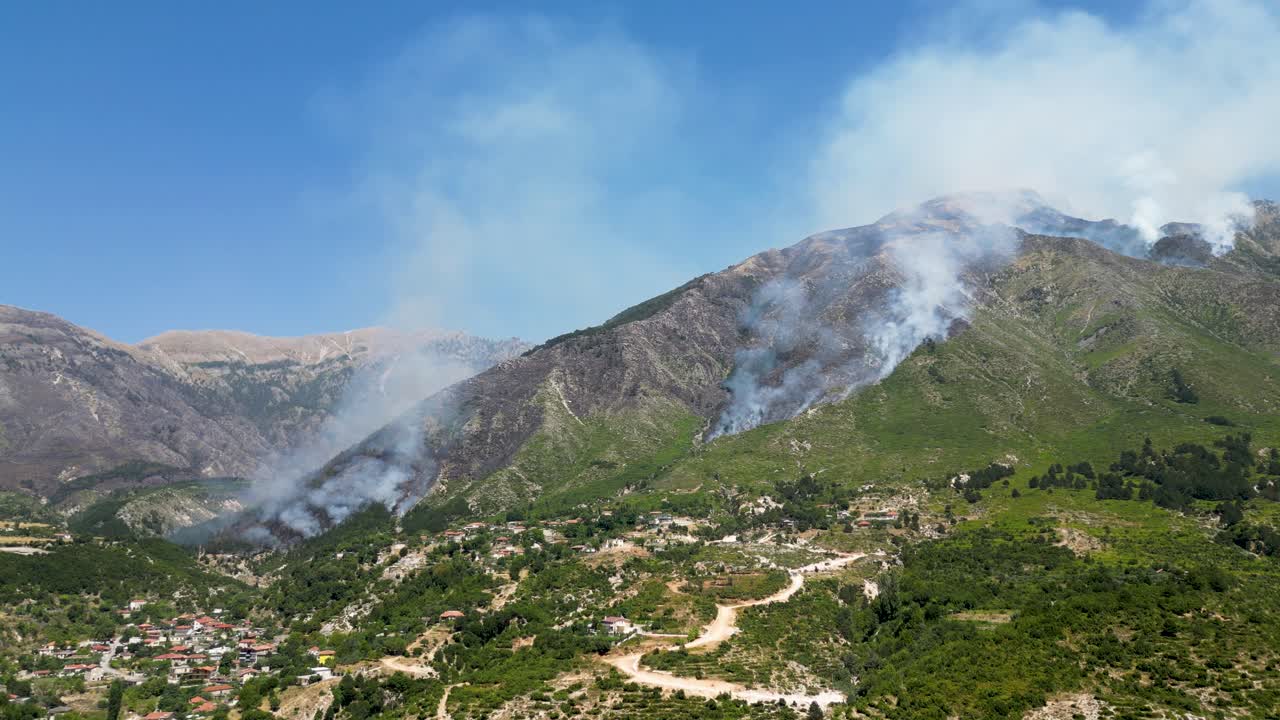 Wildfire burning forest on side of the mountain with village and houses nearby