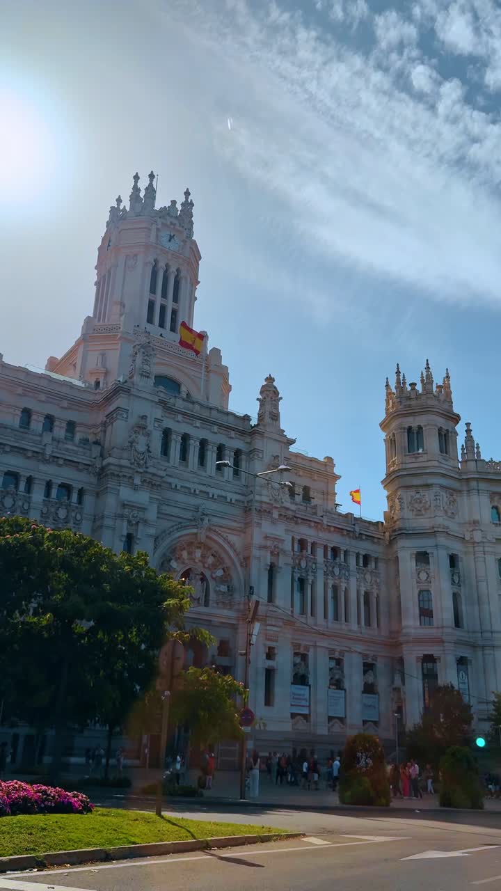 Madrid, Španělsko, 2. srpna 2025: Pamětihodnost Palacio de Cibeles pod jasným sluncem v Madridu. Vnější pohled na Palacio de Cibeles se španělskou vlajkou za mlhavého slunečního svitu a modrou oblohou s autem.