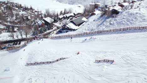 Aerial-orbit-of-a-person-ascending-the-Farellones-ski-slope-through-the-t-shaped-drag-lift,-parallax-effect-of-the-snowy-village-of-Farellones