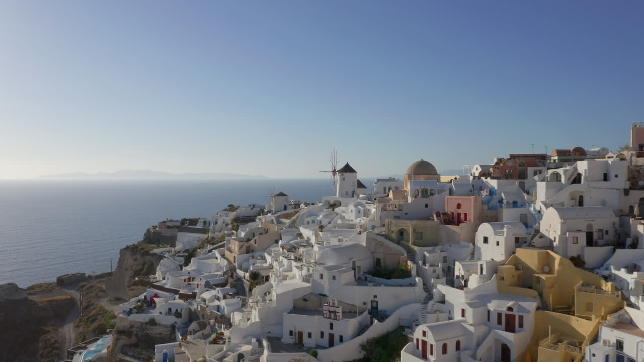 antena: drone vuela a baja altura en oia de santorini, grecia junto a los molinos de viento