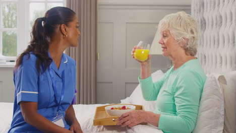 Trabajadora-De-Cuidado-Femenina-En-Uniforme-Trayendo-A-Una-Mujer-Mayor-A-Casa-El-Desayuno-En-La-Cama-En-Una-Bandeja