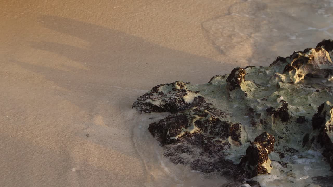 Tide pulls back on a rocky and sandy coastline. Slow-motion details of the water.