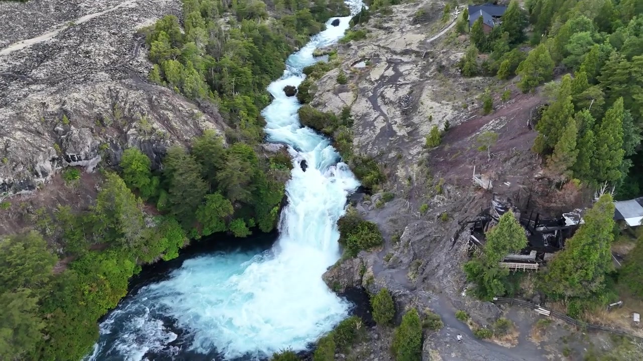 Aerial drone footage descending over the stunning Truful Truful River waterfall in Conguillio National Park. Crystal turquoise water cascades through dark volcanic lava rock canyon