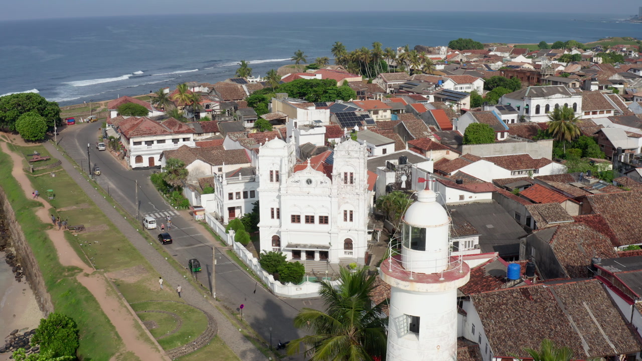 A cinematic drone sequence lowering above Galle Lighthouse with the mosque and colonial rooftops in the background, showcasing the blend of architecture and coastal heritage in Sri Lanka’s old town.