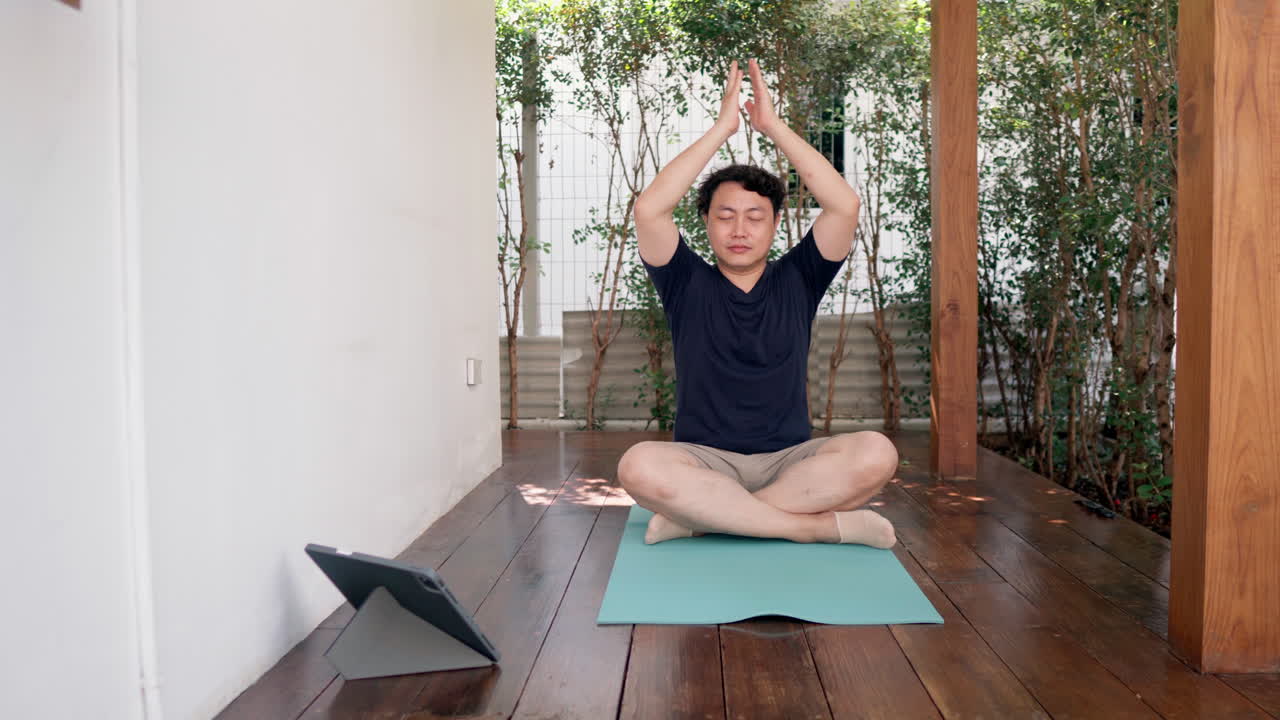 Asian man practicing mindful yoga meditation exercise with online guiding on tablet
