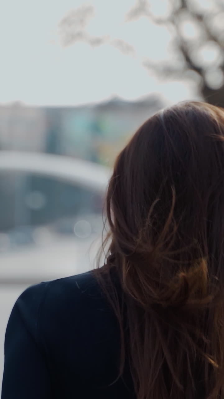 Back view of a woman walking in the autumn park with long dark hair turning back to the camera. Selective focus used in video Vertical video