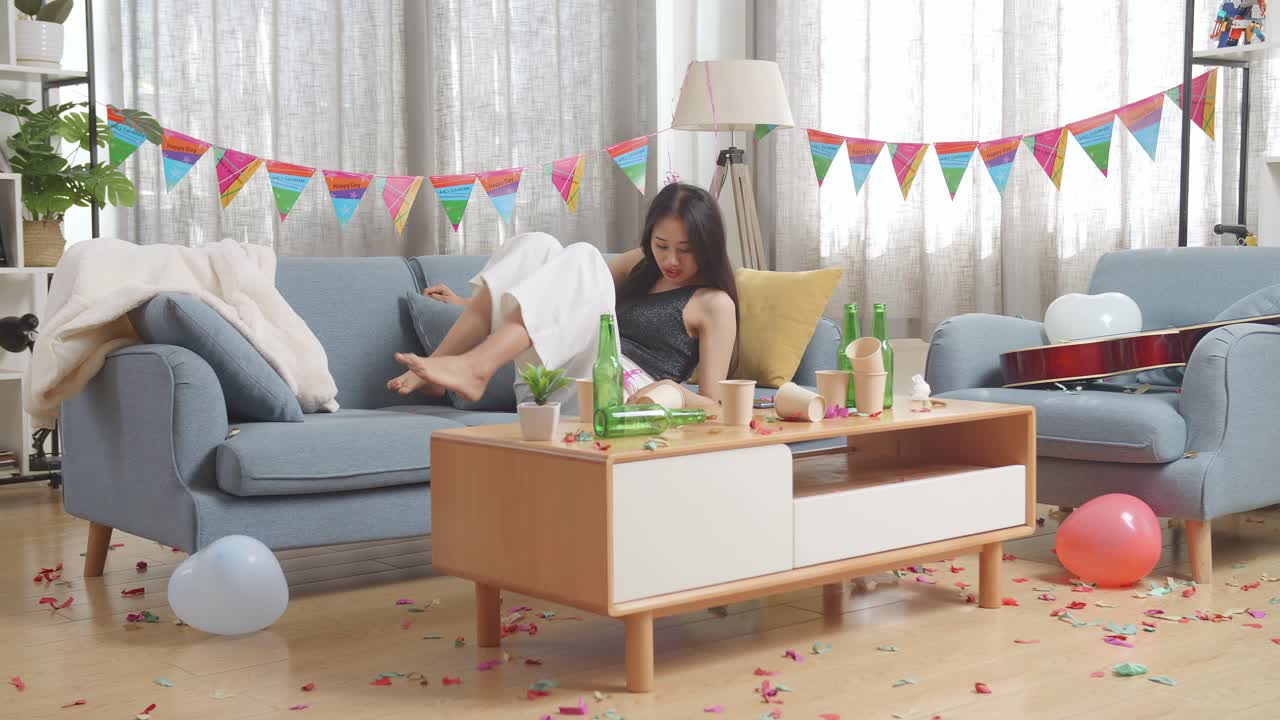 술에 취한 아시아 여성이 소파에서 잠을 자고 집에 있는 파티 에서 두통으로 인해 머리를 손으로 잡고 깨어난다.