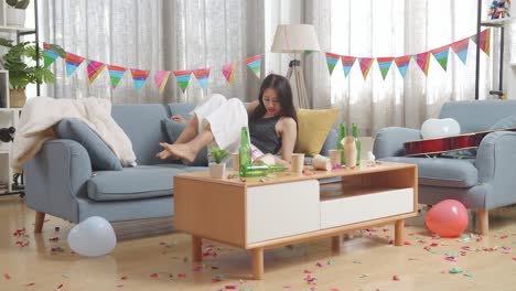 술에 취한 아시아 여성이 소파에서 잠을 자고 집에 있는 파티 에서 두통으로 인해 머리를 손으로 잡고 깨어난다.