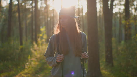 young woman with a backpack walks through serene forest, softly illuminated by warm evening sunlight from behind, with a thoughtful looks as she walk