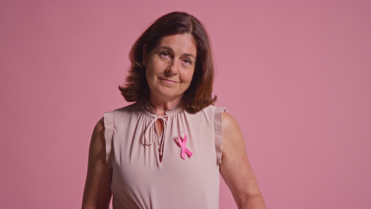 retrato de estudio de una mujer madura sonriente que lleva con orgullo ropa rosa y una cinta de concienciación sobre el cáncer de mama contra un fondo rosa 1