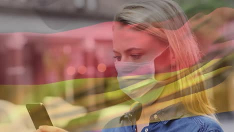 Belgium-waving-flag-against-caucasian-woman-wearing-face-mask-using-smartphone-on-the-street