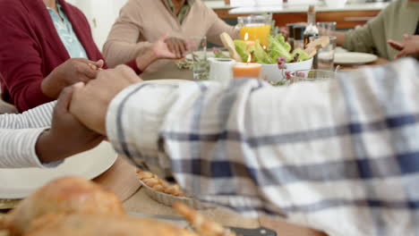 happy african american multi generation family holding hands at thanksgiving dinner, slow motion