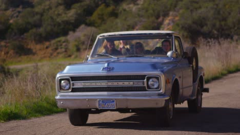 Un-Grupo-De-Amigos-En-Una-Camioneta-Azul-En-Una-Carretera-Rural