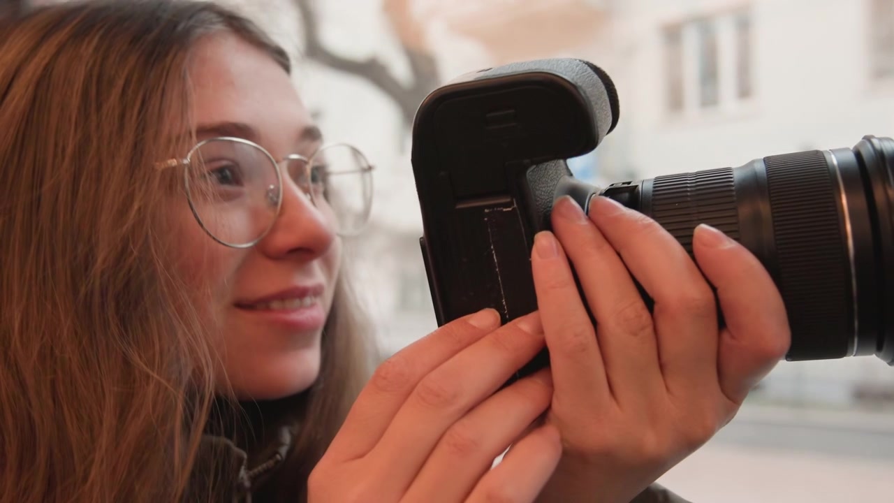 Caucasian woman with dslr camera framing city scenes, focused expression, glasses, hands adjusting lens, soft urban light, window reflections, candid enthusiast photographing architecture