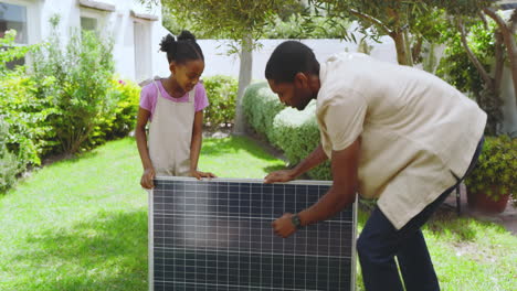 african american father and daughter examining solar panel together in garden