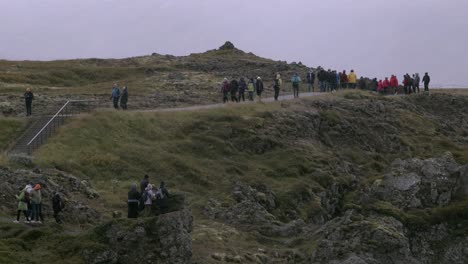 tourists walk along a rocky cliff trail in iceland on an overcast day with misty skies