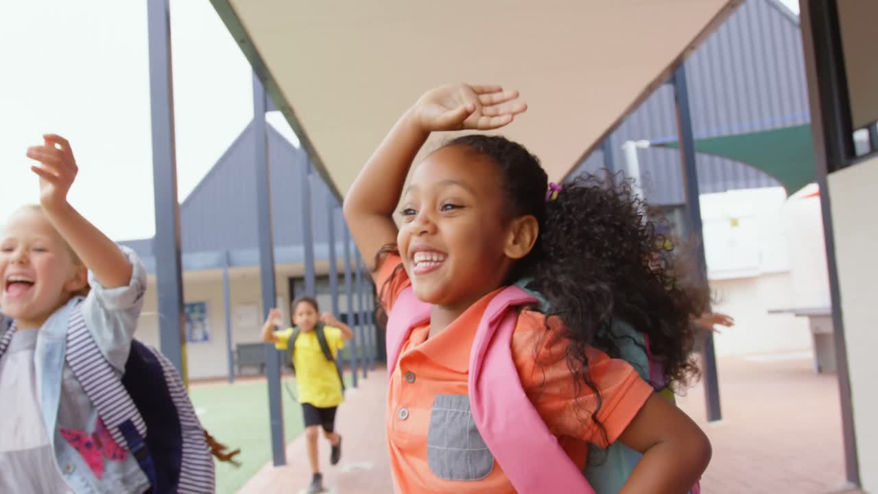 Front view of mixed-race schoolkids with schoolbags running in the corridor at school 4k