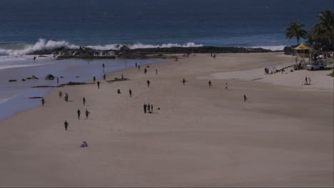 crowd of people at sandy beach with waves splashing at snapper rocks in coolangatta, qld, australia. wide shot