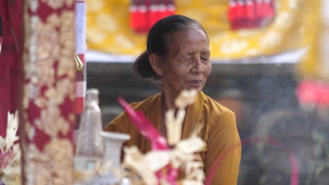 bright decorations, flowers and offerings frame elderly woman at hindu temple in bali, indonesia