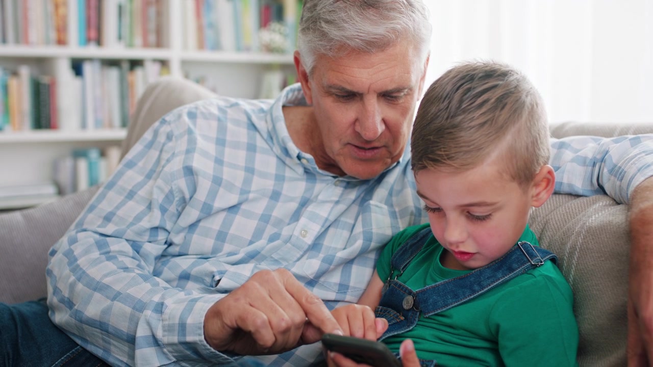 Grandfather and Grandson Using Smartphone Together on Sofa