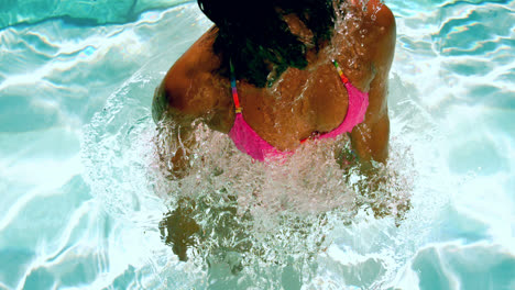 mujer feliz en bikini rosa sacudiendo el cabello mojado en la piscina