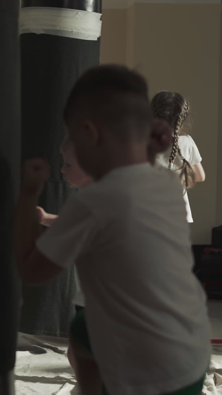 Children group trains with punching bags in martial arts class. Little fighters exercises kicking heavy inventory in sports school slow motion