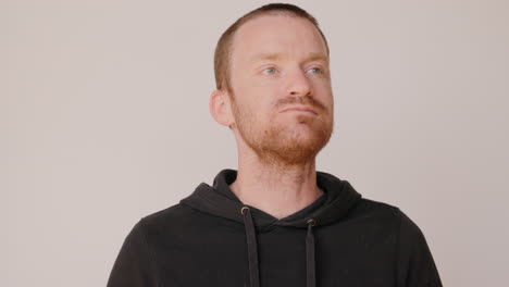 red haired man in a dirty hoodie eating a piece of pizza and crust on a white backdrop