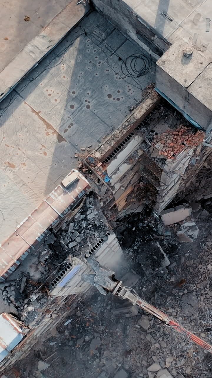 Edificio alto destruido. Máquina de demolición derribando el techo de un edificio en ruinas. Garra larga de máquina retirando los escombros. Video vertical