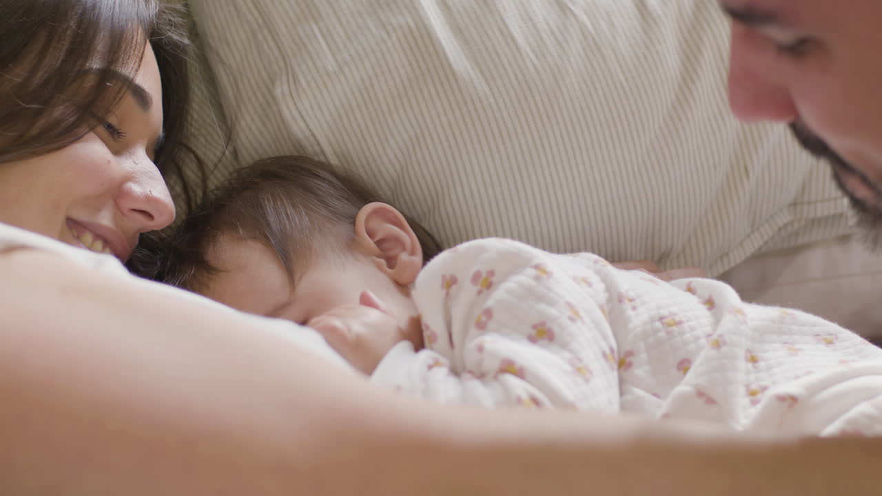 primer plano de papá y mamá felices abrazando a su hijita mientras están acostados en la cama el domingo por la mañana