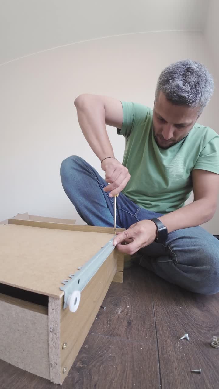 Uomo che assembla mobili con un cacciavite su un pavimento in legno.