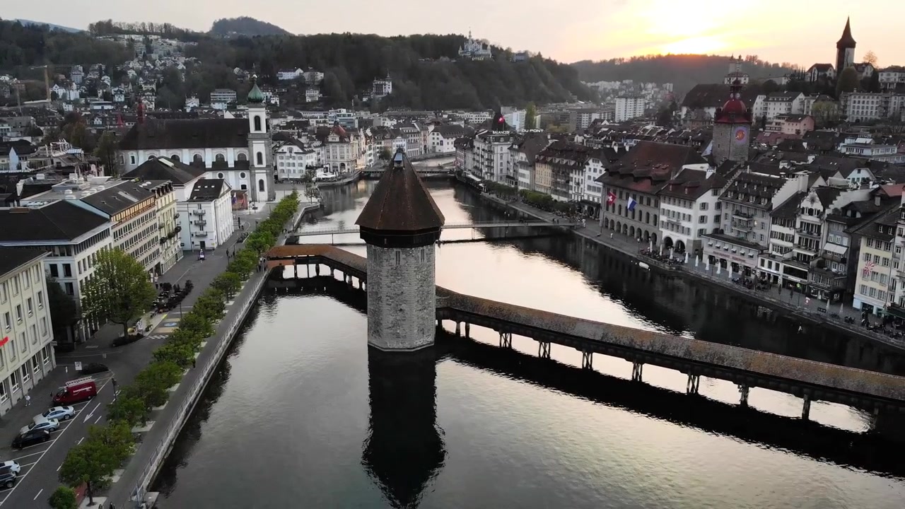 Vista aérea de Lucerna, Suíça, ao pôr do sol, com uma panorâmica ascendente em direção à histórica Altstadt, afastando-se da ponte Kappelbrücke