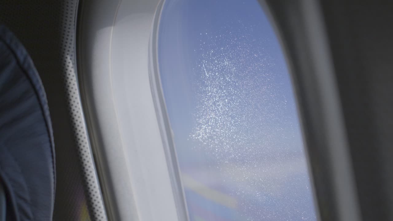 An airplane window showing blue sky with a scattered water residue, aerial view