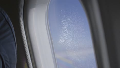 an airplane window showing blue sky with a scattered water residue, aerial view