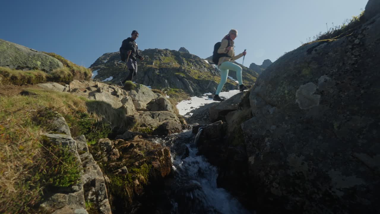Escursionisti saltano un piccolo ruscello tra grandi massi con uno sfondo montuoso in Norvegia, catturando un momento attivo e avventuroso all'aperto nella natura