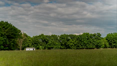 timelapse of stormy clouds changing to sunshine over field of grass and trees on windy day