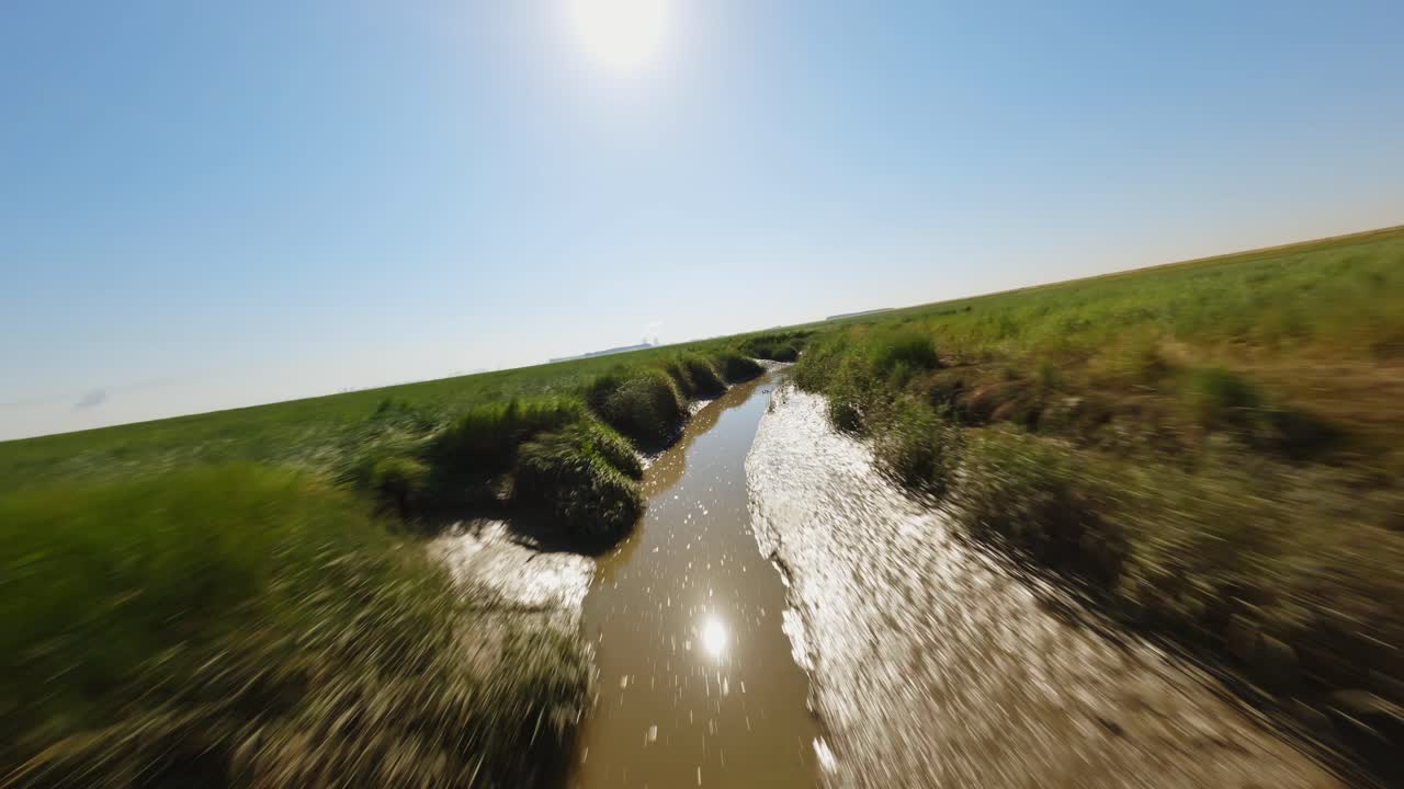 fpv drone disparó volando sobre un arroyo fangoso y estrecho a través de humedales verdes debajo de un cielo azul claro de verano