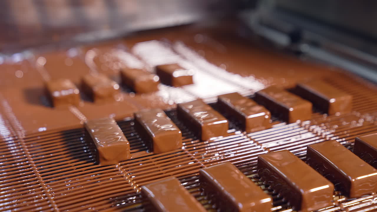 Appetizing freshly-covered with chocolate glazing sweets. Candies poured with chocolate icing. Sweet food production line.
