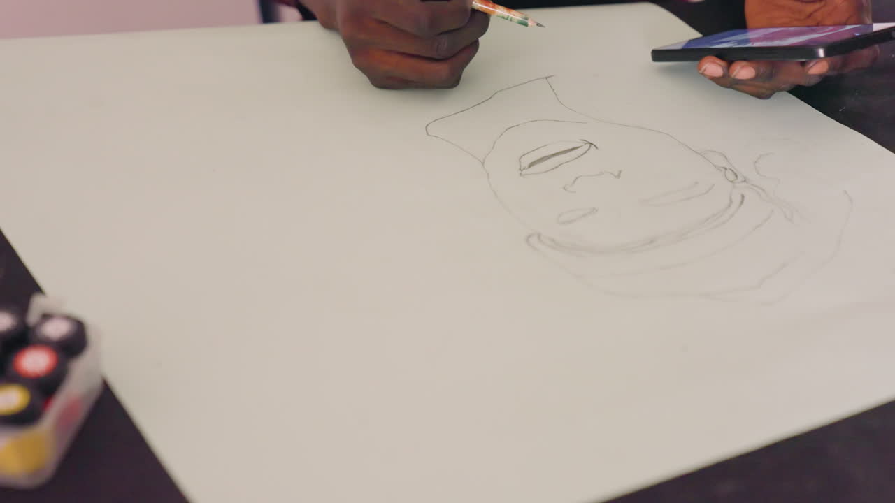 Black artist sketching portrait on paper using pencil and smartphone reference, dotted outline forming face, paint palette at table corner, closeup of darkskinned hands, calm focused studio