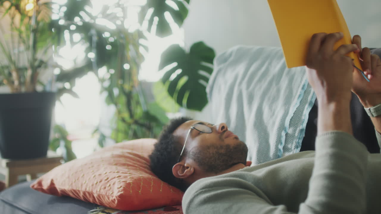 Young Man Lying on Sofa and Reading Book