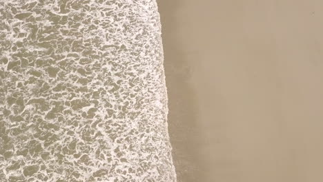 top down, birds eye view shot of shoreline waves on beach