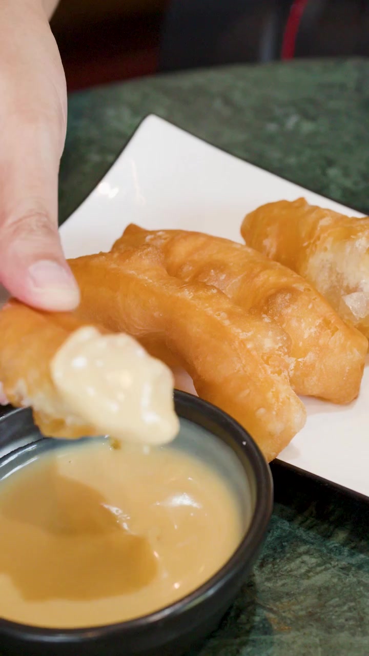 Primo piano di mani che intingono pasta fritta dorata nel latte condensato dolce su marmo verde.